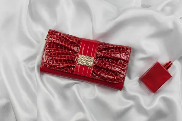 Tasche aus lackiertem Leder und rotem Parfüm auf weißer Seide liegend. Handtasche für Frauen und Duftflasche, Draufsicht. — Stockfoto