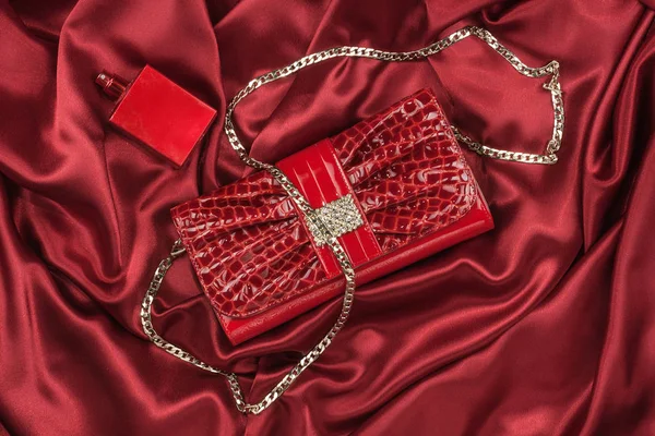 Tasche aus lackiertem Leder und rotem Parfüm auf roter Seide liegend. Handtasche für Frauen und Duftflasche, Draufsicht. — Stockfoto