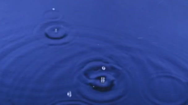 Close-up vallende druppels regen in blauw water. — Stockvideo