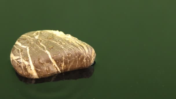 Gota de agua cayendo sobre una piedra marrón yaciendo en agua verde . — Vídeos de Stock