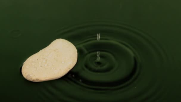 Μια σταγόνα που πέφτει στο πράσινο νερό κοντά την άσπρη πέτρα. — Αρχείο Βίντεο