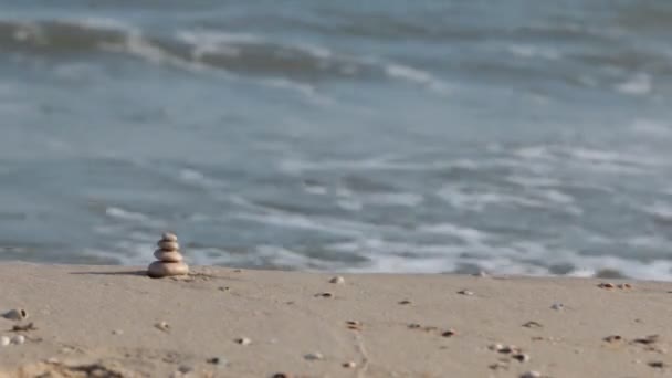 Piramide gemaakt van witte stenen tegen de achtergrond van de golven van de zee. — Stockvideo