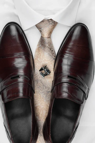 Pair of classic brown shoes standing on a shirt and tie. Men's fashion. — Stock Photo, Image