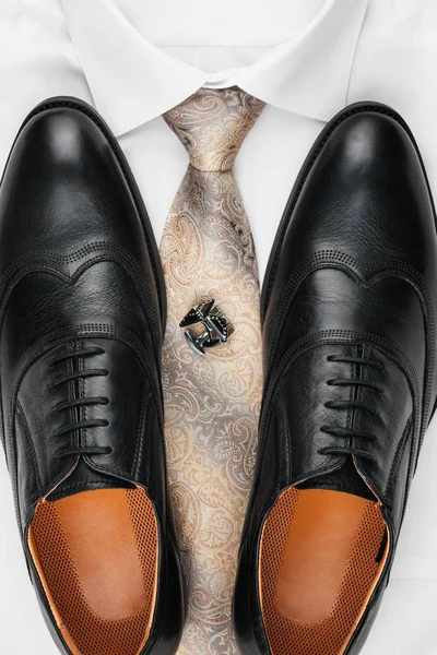 Ζευγάρι κλασικά μαύρα παπούτσια που στέκεται πάνω σε ένα πουκάμισο και γραβάτα. Μόδα ανδρών. — Φωτογραφία Αρχείου