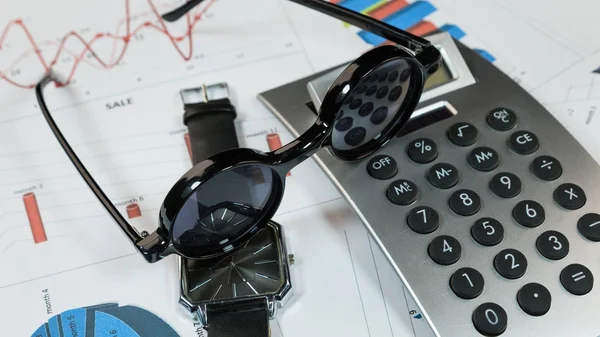 Sluneční brýle, hodiny a kalkulačka leží na pozadí diagramů. Myšlenky a koncepty podnikání. — Stock fotografie