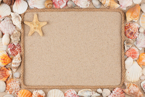 Beautiful frame made of rope and star, sea shells on the sand, with place for your image, text.