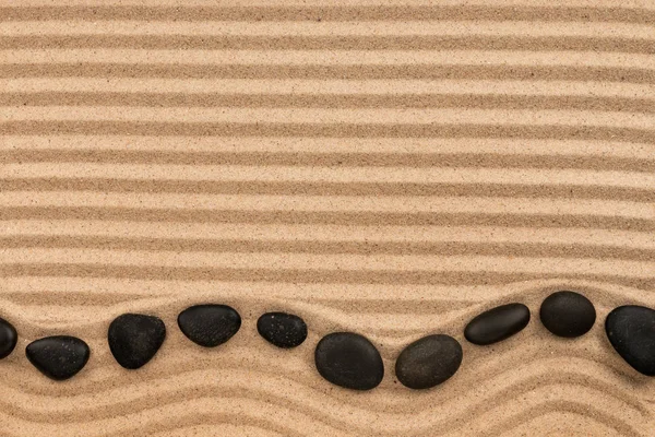 Πλαίσιο κατασκευασμένο από μαύρες πέτρες ξαπλωμένος ζιγκ-ζαγκ, σε σπαστά άμμο. — Φωτογραφία Αρχείου
