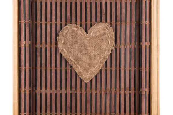 Καρδιά από λινάτσα βρίσκεται σε ένα χαλί μπαμπού με καμπύλες άκρες. — Φωτογραφία Αρχείου
