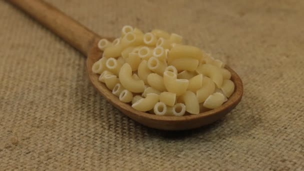Close-up, lepel vruchtwisseling met een stapel van macaroni liggend op jute. — Stockvideo
