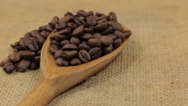 Rotación, montón de granos de café cayendo de una cuchara de madera en la arpillera . — Vídeos de Stock