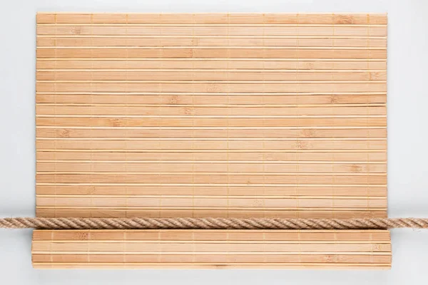 Estera de bambú con bordes rizados y cuerda, acostada sobre un fondo blanco . — Foto de Stock
