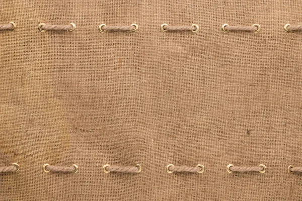 Texture of burlap with two ropes inserted in gold rings. Frame — Stock Photo, Image