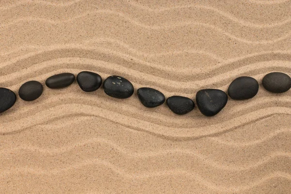 Γραμμή, κατασκευασμένο από μαύρες πέτρες ξαπλωμένος κυματιστές, σε άμμο αμμόλοφος. — Φωτογραφία Αρχείου