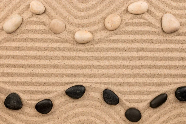 Dva řádky z černé a bílé kameny ležící na písku, s prostorem pro text. — Stock fotografie