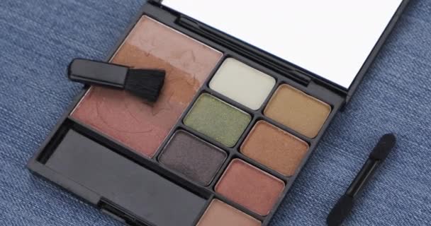 Rotation of cosmetic lying on denim. Eyeshadow and brush. — Stock Video