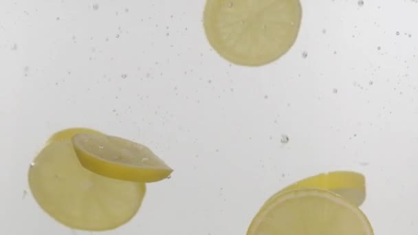 En cámara lenta. Limón fresco en rodajas que cae al agua con salpicaduras y burbujas sobre fondo blanco . — Vídeos de Stock