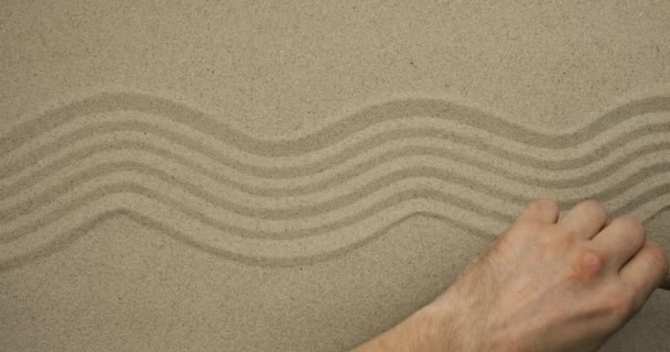 Mão masculina desenha linhas de ondas na areia. Vista superior . — Vídeo de Stock