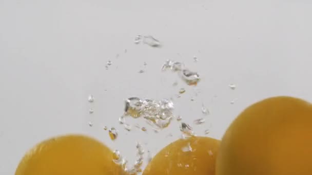 Naranjas enteras caen al agua con burbujas. Movimiento lento . — Vídeo de stock