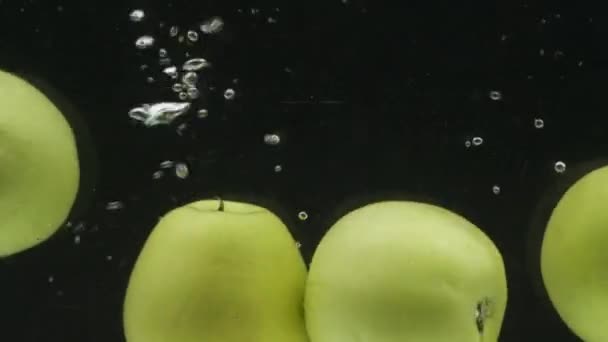 Hele groene appels vallen in het water met belletjes. Langzame beweging. — Stockvideo