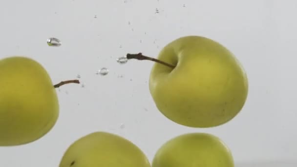 Ganze grüne Äpfel fallen mit Blasen ins Wasser. Zeitlupe. — Stockvideo