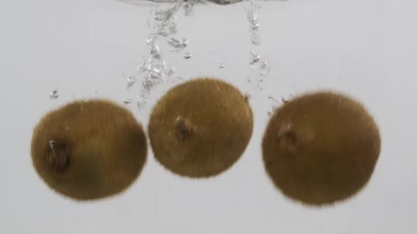 Celé kiwi padají do vody s bublinkami. Zpomalený pohyb. — Stock video