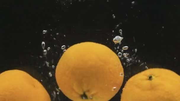 Celé mandarinky padají do vody s bublinkami. Zpomalený pohyb. — Stock video