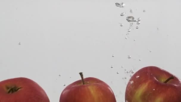 Ganze rote Äpfel fallen mit Blasen ins Wasser. Zeitlupe. — Stockvideo