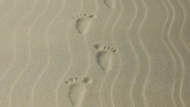 Zooma in. Stiliserade fotspår av en person, som sträcker sig ut i fjärran. Fotspår i sanden. — Stockvideo