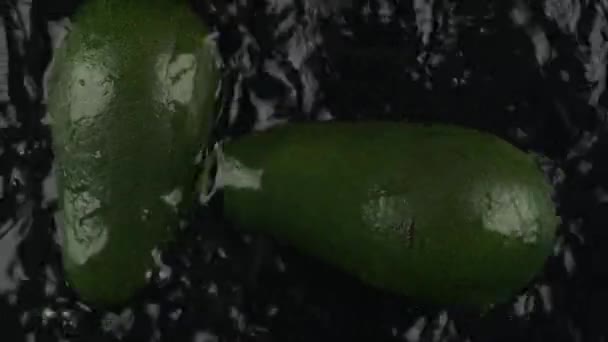 Zeitlupe. Zwei Avocadohälften fallen in Wasser auf schwarzem Hintergrund. Ansicht von oben. — Stockvideo