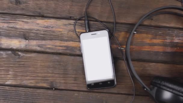 Schwarze Kopfhörer und Smartphone auf Holztisch. Kranichschuss. Ansicht von oben. — Stockvideo