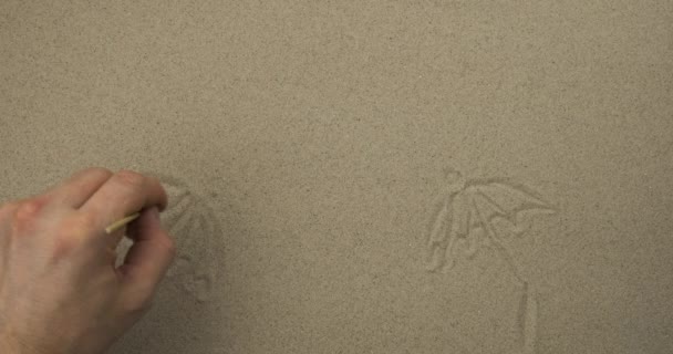 Ζωγραφίζοντας με ένα ραβδί στην άμμο. Ομπρέλες στο φόντο της θάλασσας, του ήλιου και των πουλιών. — Αρχείο Βίντεο