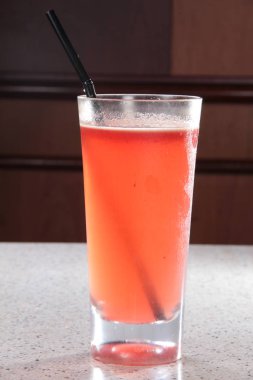 red cocktail in glass with ice and straw on the table close up