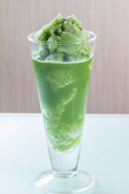Beyaz arka planda cam bardakta yeşil içecek.