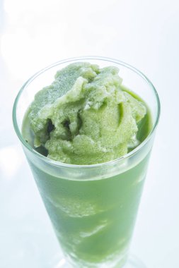 Beyaz arka planda cam bardakta yeşil içecek.