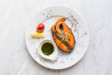 Bir plaka üzerinde otlar, limon, domates ve salsa soslu somon steak. Üstten Görünüm.