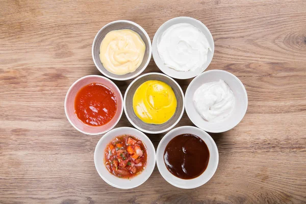 Set of sauces - ketchup, mayonnaise, mustard soy sauce, bbq sauce, mustard grains and pomegranate sauce on wooden table — Stock Photo, Image