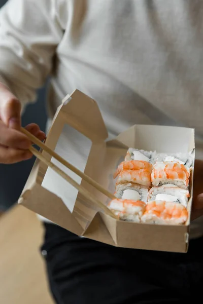 Homem comendo filadélfia rolo com camarões pauzinhos de caixa de artesanato. serviço de entrega de rolos de comida japonesa em caixa de artesanato — Fotografia de Stock