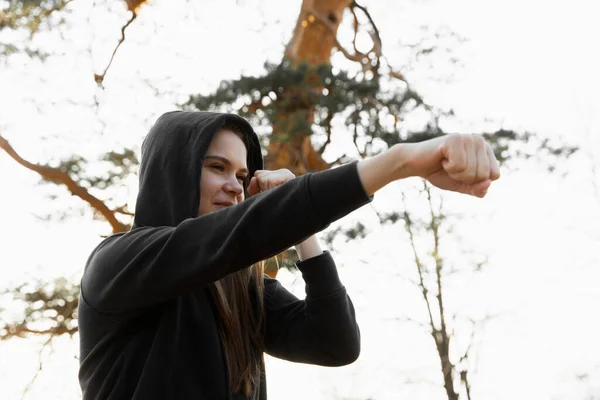 Ung idrottskvinna boxning i parken. Ung kvinna tränar en direkt träff, fokus på ögonen Stockfoto
