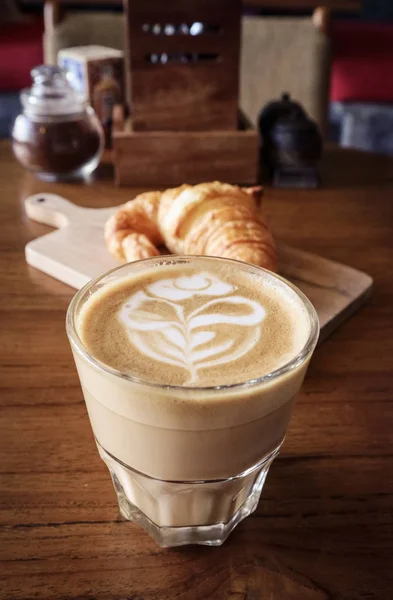 Šálek kávy s latte art na vrcholu a máslový croissant — Stock fotografie