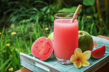 Guava smoothie in glass with bamboo drinking straw and fresh guava on tray outdoo clipart