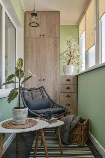 Interior of cozy balcony with green walls, sitting area with rug, armchair and two coffee tables