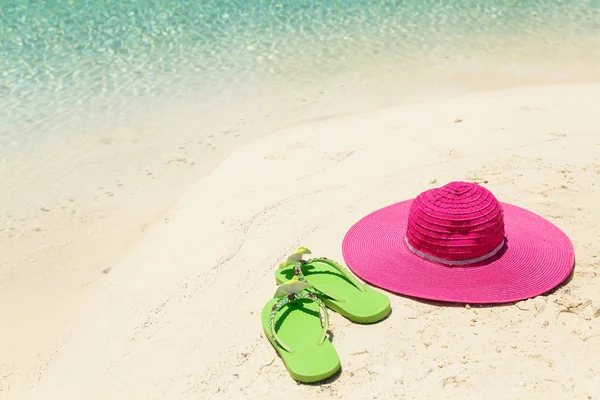 Cappello da spiaggia rosa e pantofole verdi nella sabbia dorata dal mare shor — Foto Stock