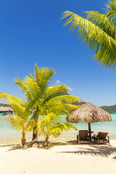 Two sunlounger chairs under a thatched parasol on a sand beach w — Stock Photo, Image