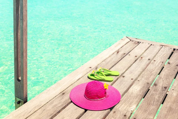 Grande cappello da sole rosa e flip plops verde sul ponte in riva al mare — Foto Stock