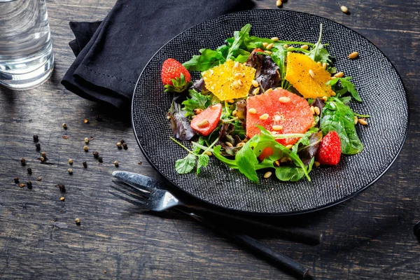 Pompelmo e arancia mescolano insalata con pinoli su piatto nero un — Foto Stock