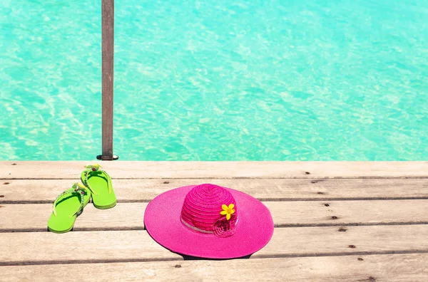 Grote roze zon hoed en groene sandalen op het dek aan zee — Stockfoto