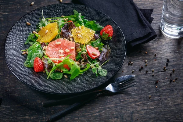 Pompelmo e arancia mescolano insalata con pinoli su piatto nero un — Foto Stock