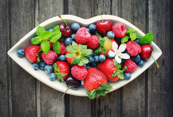 Mix of fresh berries in white plate in shape of lips, on wooden — Stock Photo, Image