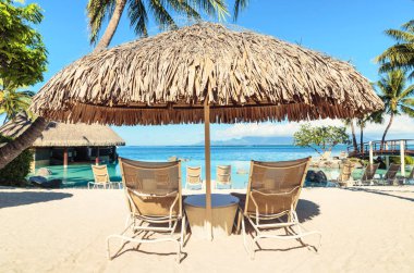 İki güneş-şezlong ve Tiki hut güneş şemsiyesi tropikal plaj