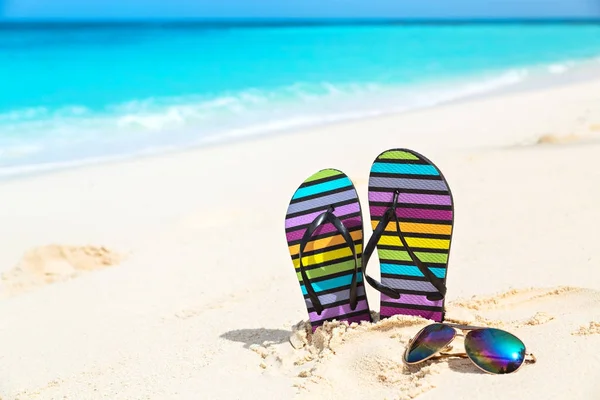 Chanclas multicolores y gafas de sol en una playa soleada —  Fotos de Stock